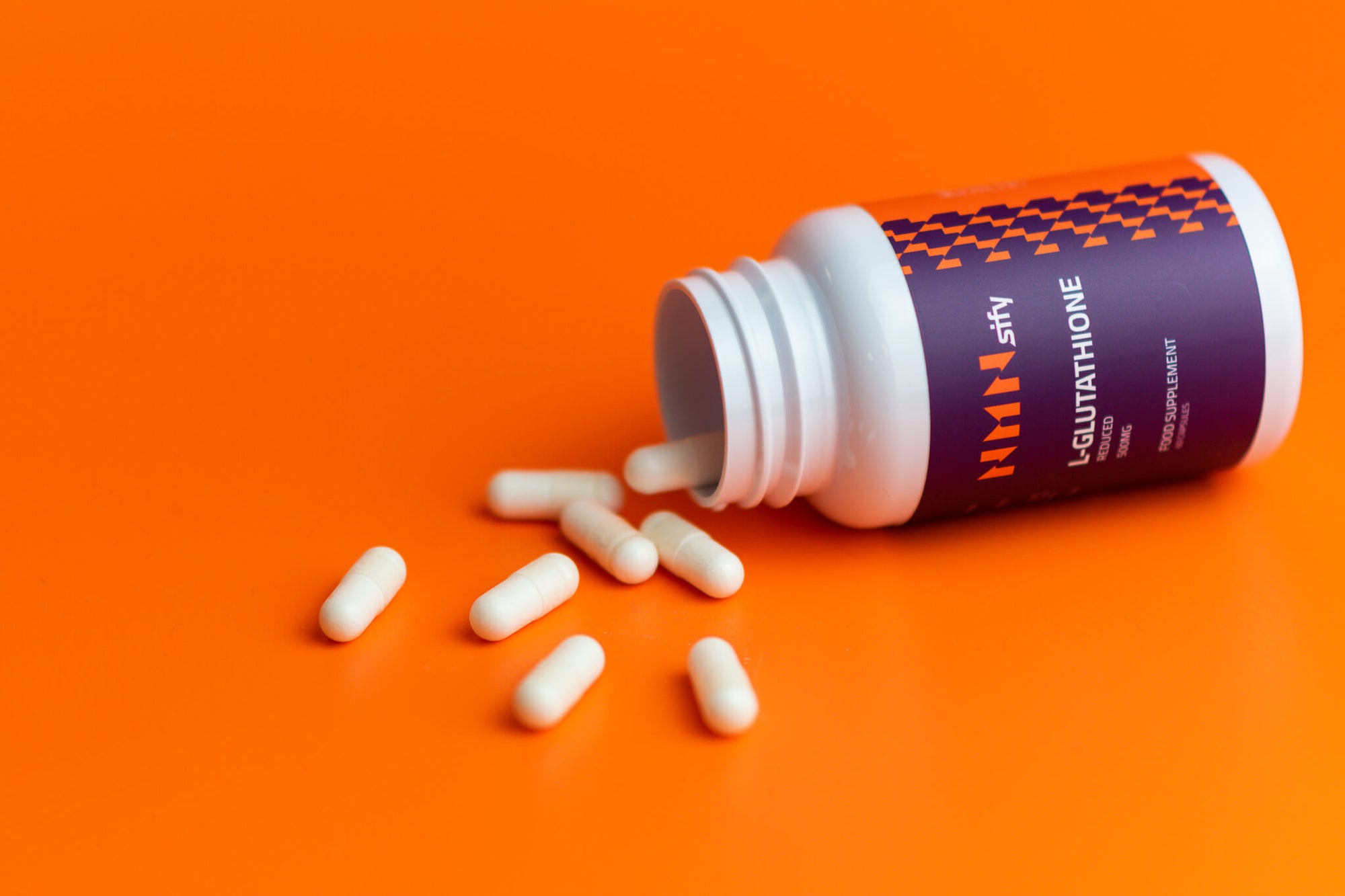 Glutathione-supplement-bottle-with-falling-capsules-orange-background